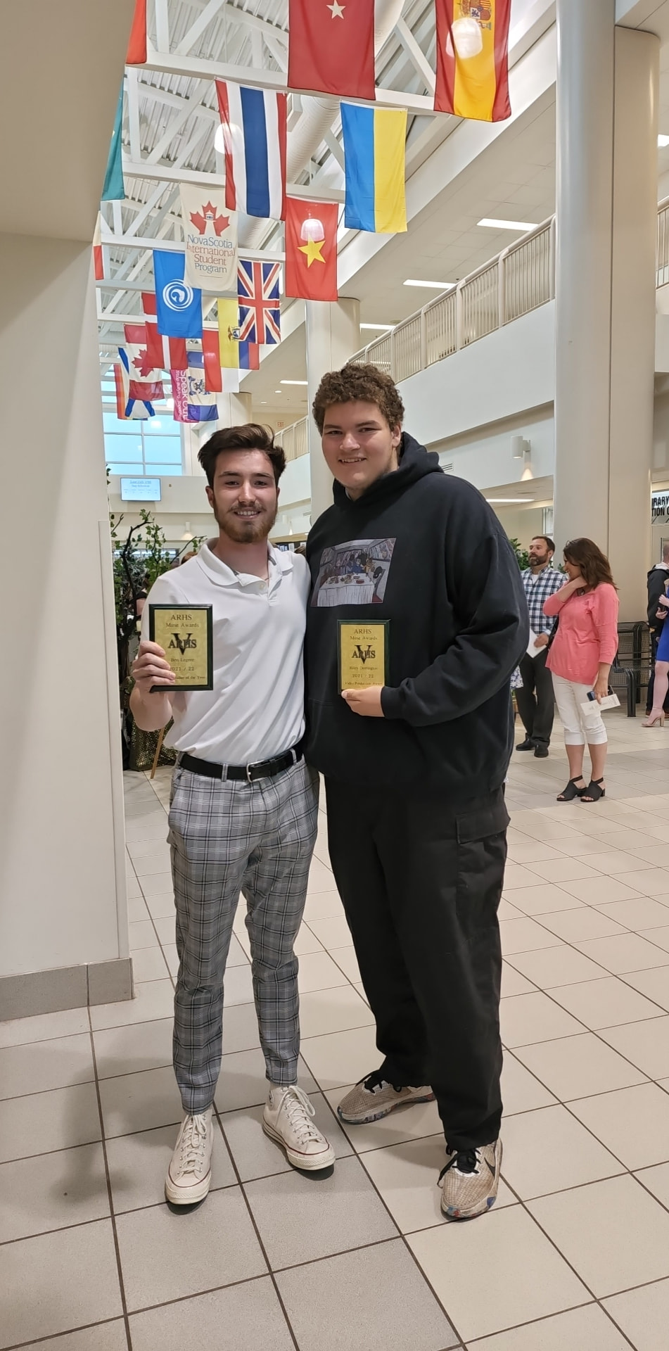 Two filmmakers holding awards at a school ceremony