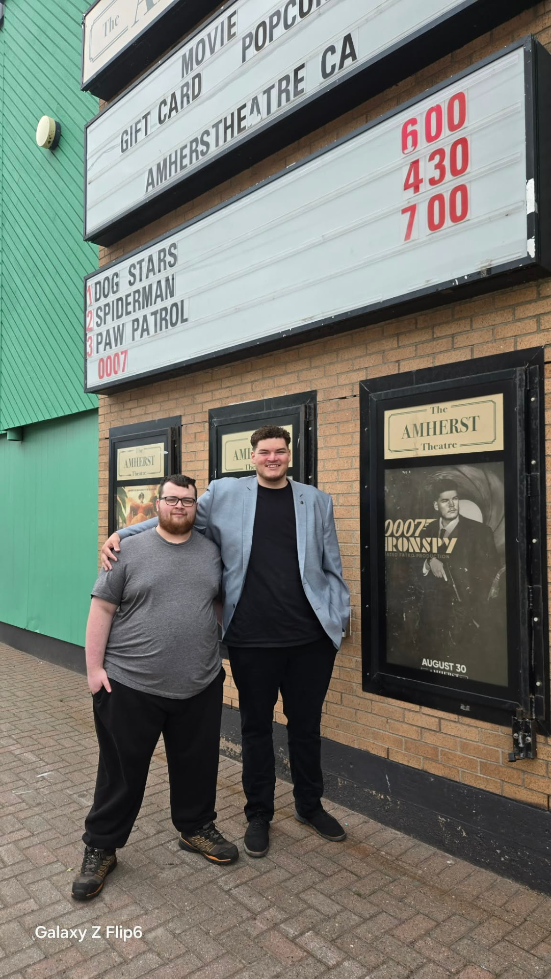 Two crew members outside the Amherst Theatre beside the 0007 Ironspy poster
