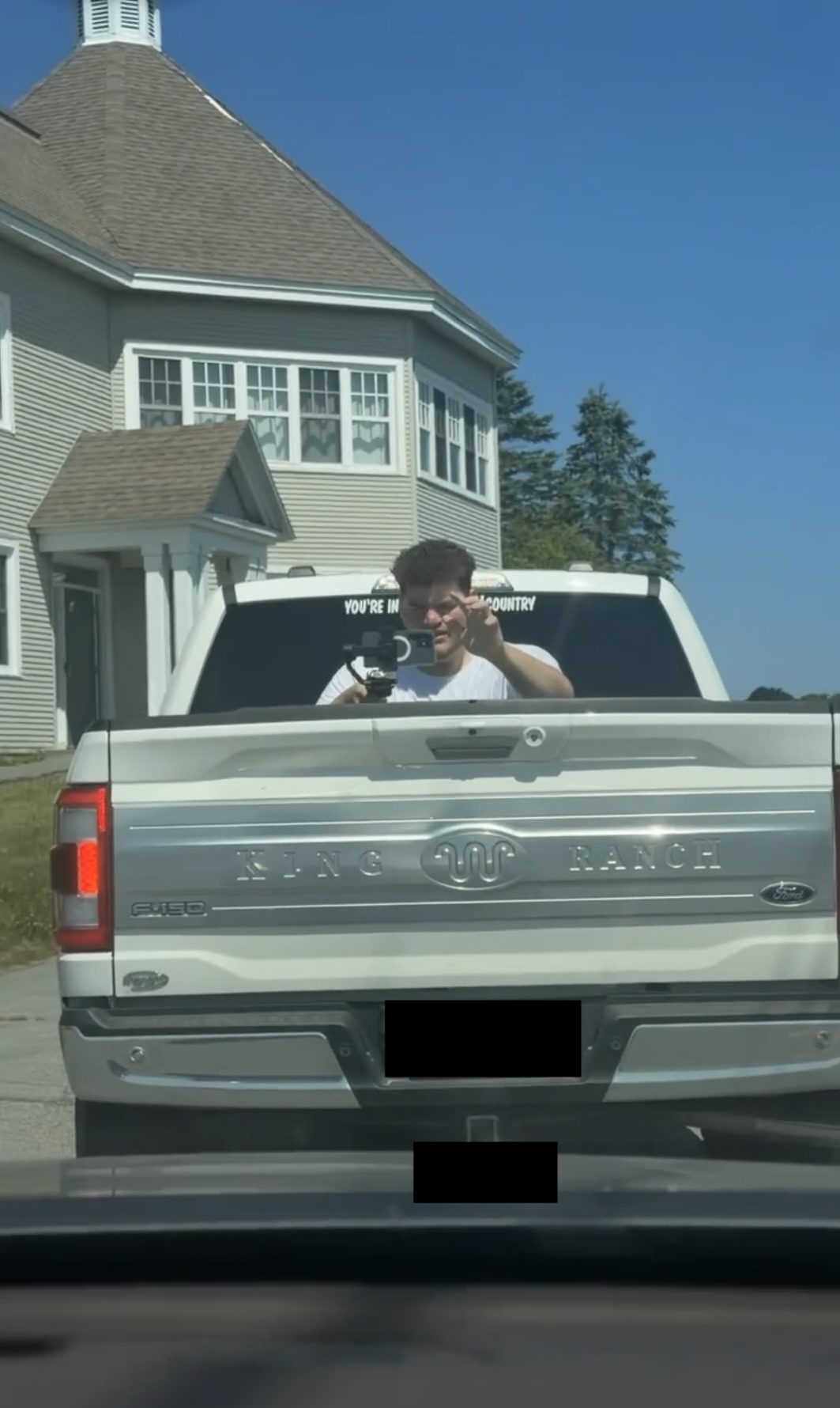 Camera operator reflected in a pickup truck window during location filming