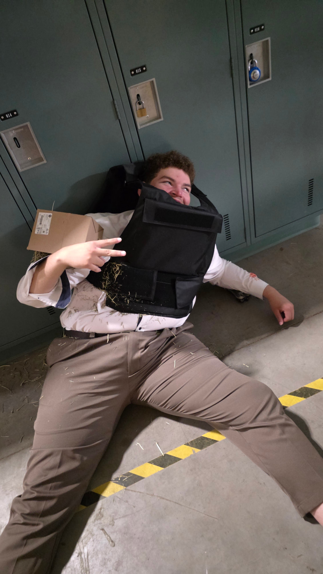 Actor wearing a protective vest lying on the floor beside lockers